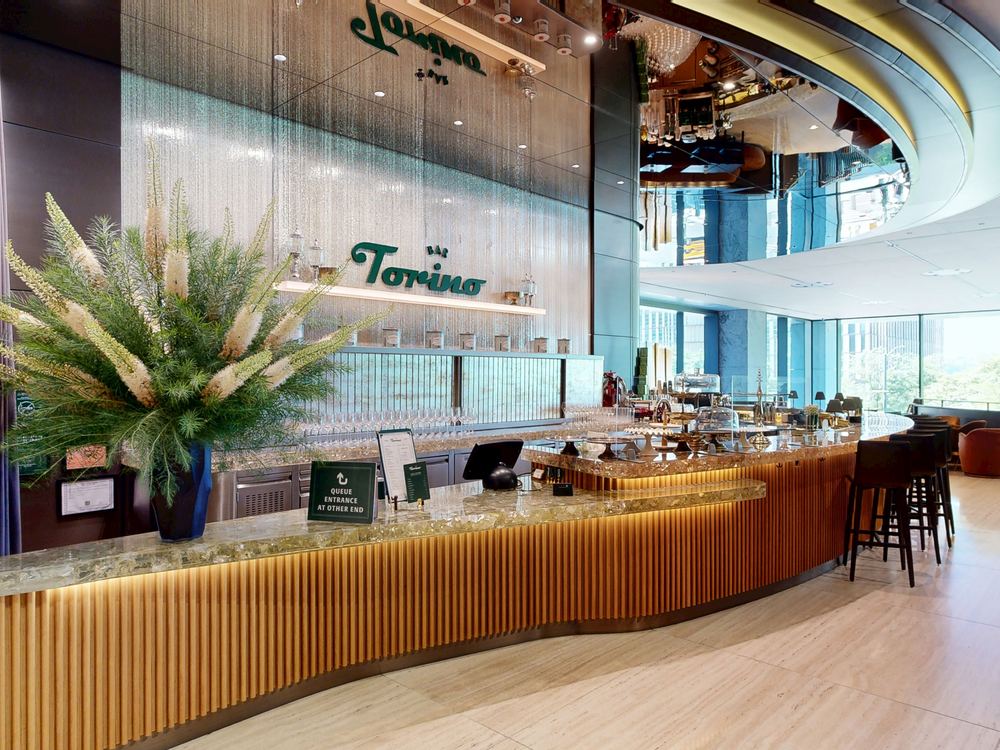 Bar Torino's marble and wood bar counter at 50 Hudson Yards in New York City, with the restaurant's logo displayed above the back bar
